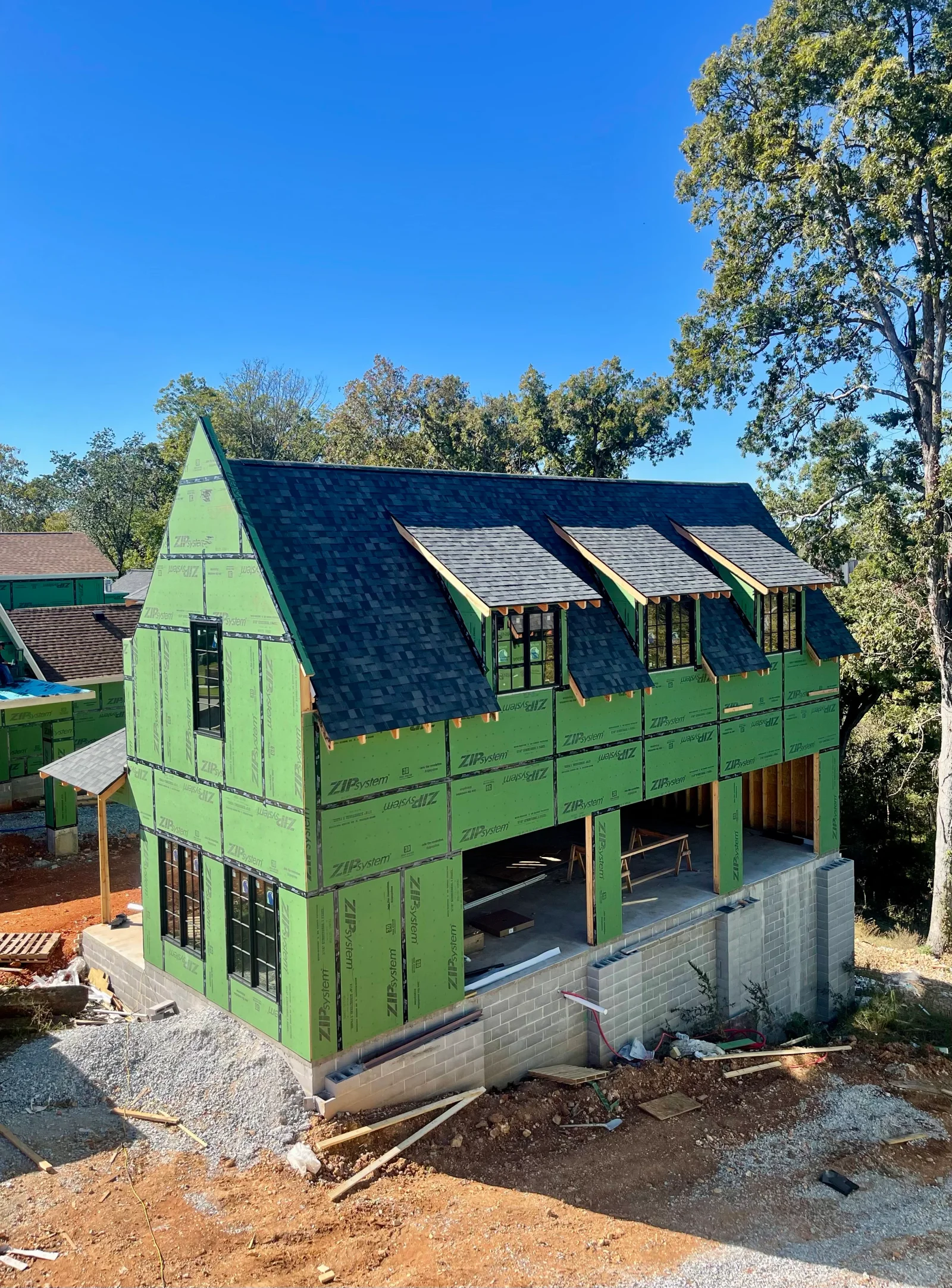 Dark architectural shingles installed on multi-plane residential roof with dormers and brick foundation